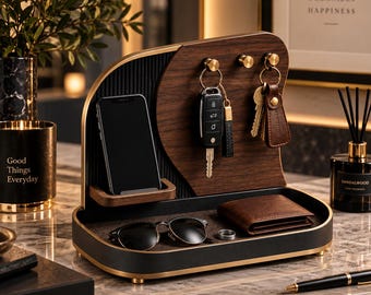 May include: A desk organizer featuring a dark wood grain panel with three gold-toned hooks for keys, a vertical slot for a smartphone, and a black tray base. The tray holds a brown leather wallet, black sunglasses, and a silver ring.
