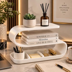 May include: A white S-shaped desk organizer with three tiers. The top tier holds a small succulent in a gray pot and a brown glass diffuser bottle labeled CALM. The middle tier holds three books titled KINFOLK, Minimalista, and LIVE BEAUTIFUL.