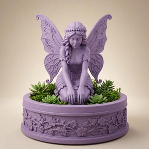 May include: A lavender-colored fairy figurine with large, intricate wings, kneeling in a circular planter. The planter features a relief pattern of flowers and vines around its exterior, and the interior is filled with green succulents and moss.