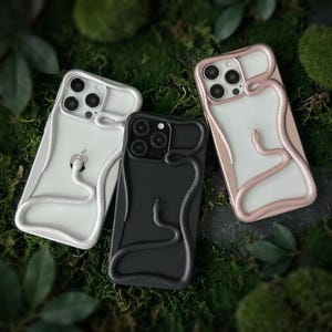 May include: Three smartphone cases featuring a raised, three-dimensional snake design that wraps around the camera module and across the back. The set includes one white case with a white snake, one black case with a black snake, and one rose gold case.