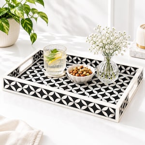 Puede incluir: Una bandeja de servicio rectangular con un patrón geométrico en blanco y negro de círculos y diamantes entrelazados. La bandeja tiene lados elevados con asas integradas y un acabado liso, mostrando un motivo repetitivo en toda su superficie.