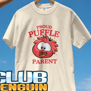 May include: An ivory short-sleeve t-shirt featuring a red graphic of a round, fuzzy creature with the text PROUD PUFFLE PARENT above and below the character. The shirt includes small star accents and the text CLUB PENGUIN at the bottom.