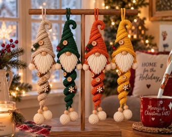 May include: Four crochet gnome ornaments hanging from a wooden stand. Each gnome features a pointed hat, a white yarn beard, and a long, spiraling body ending in two white pom-poms. The gnomes are beige, green, orange, and yellow with wooden buttons.