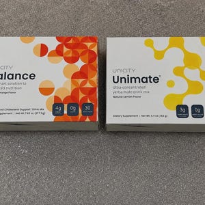 May include: Two rectangular boxes of Unicity dietary supplements. The left box is labeled Balance, Natural Orange Flavor, with orange circular patterns and 217.5g net weight. The right box is labeled Unimate, Natural Lemon Flavor, with yellow organic shapes and 153g net weight.