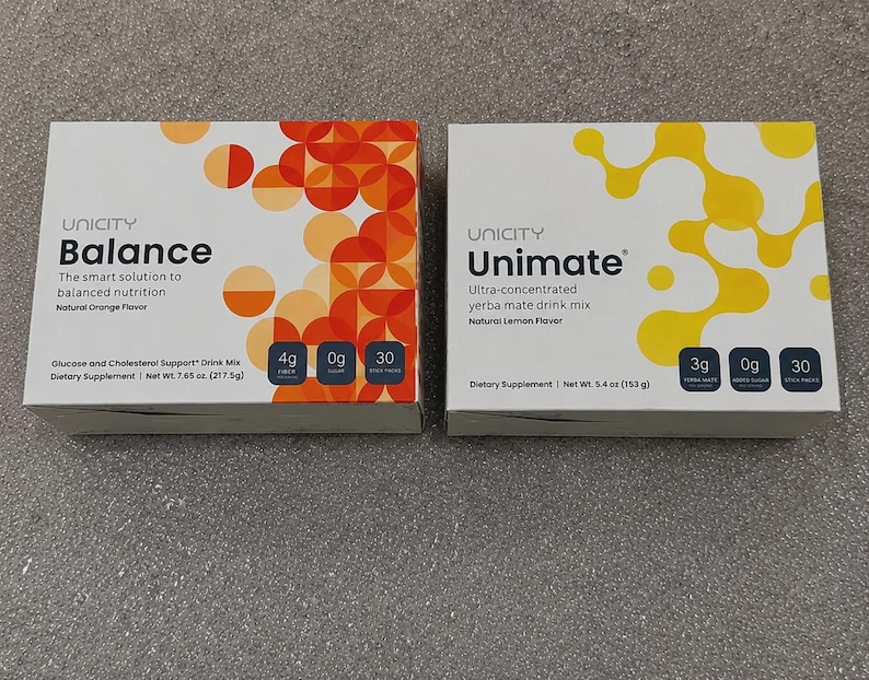May include: Two rectangular boxes of Unicity dietary supplements. The left box is labeled Balance, Natural Orange Flavor, with orange circular patterns and 217.5g net weight. The right box is labeled Unimate, Natural Lemon Flavor, with yellow organic shapes and 153g net weight.