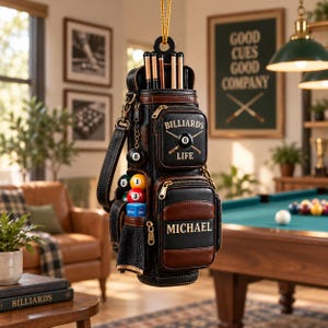 May include: A black and brown leather-style billiards cue case with a shoulder strap, featuring a top compartment for cues, two front zipped pockets, and side storage for billiard balls and chalk. The text "BILLIARDS LIFE" and "MICHAEL" are printed on the front pockets.