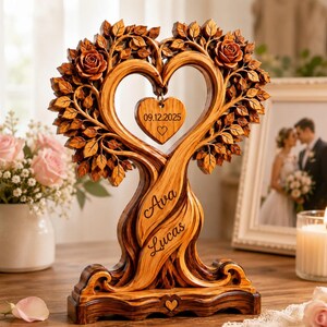 May include: A wooden heart-shaped tree sculpture featuring carved roses and leaves. A small heart pendant hangs in the center with the date 09.12.2025. The trunk is engraved with the names Ava and Lucas, and a small heart is carved into the base.