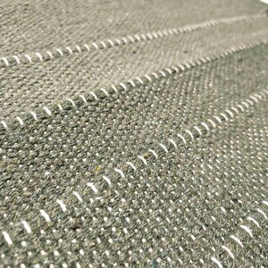 May include: A textured olive green woven fabric featuring horizontal rows of white stitched detailing. The material has a dense, nubby surface with a consistent pattern of parallel lines running across the length of the textile surface.