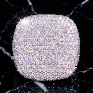 Peut inclure: Une bague de forme carrée présentant un sertissage pavé dense composé de nombreuses petites pierres claires taille brillant qui recouvrent toute la surface supérieure, créant un aspect étincelant et très réfléchissant avec un bord en métal argenté.