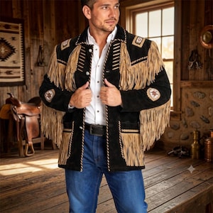 Puede incluir: Una chaqueta de ante negro con largos flecos de color tostado en el pecho, las mangas y los bolsillos. La chaqueta incluye parches circulares decorativos en los hombros y las mangas, sobre una camisa blanca y pantalones vaqueros azules.