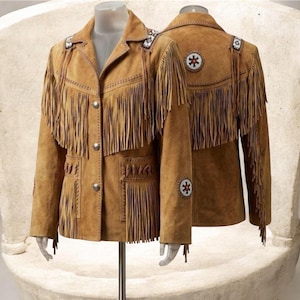 Puede incluir: Una chaqueta de ante color tostado con largos flecos en el pecho, los hombros y los bolsillos. La chaqueta incluye botones plateados, costuras decorativas y parches circulares de cuentas con un patrón de estrella en los hombros y mangas.