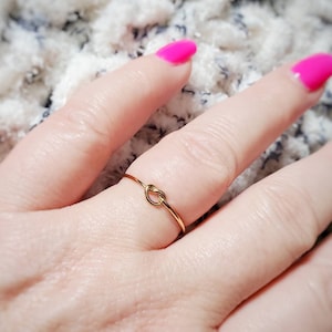 Puede incluir: Un anillo de nudo de oro simple. El anillo es delgado y delicado, con un pequeño nudo en el centro.