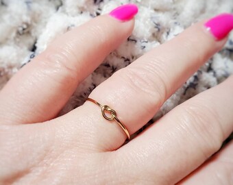 Puede incluir: Un anillo de nudo de oro simple. El anillo es delgado y delicado, con un pequeño nudo en el centro.