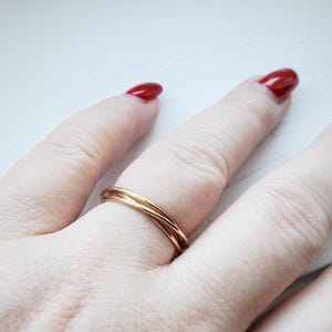 May include: A gold-toned triple band ring worn on a finger with red nail polish.