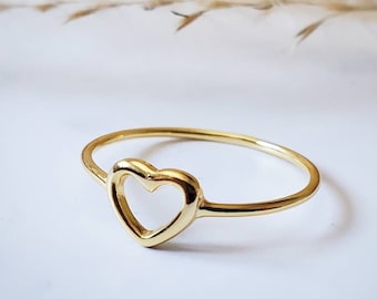 May include: A simple gold ring with a heart-shaped cutout. The ring is delicate and minimalist.