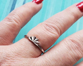 May include: A silver ring featuring a sunburst design. The ring is worn on a finger with red nail polish. The ring's sunburst design is centered on the top of the ring, with rays fanning out.