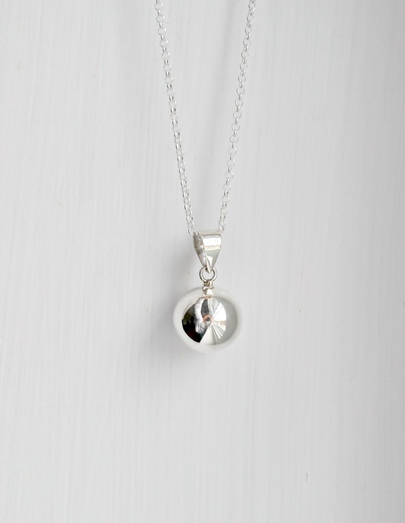 May include: A silver chain necklace with a round silver pendant. The pendant is smooth and shiny.