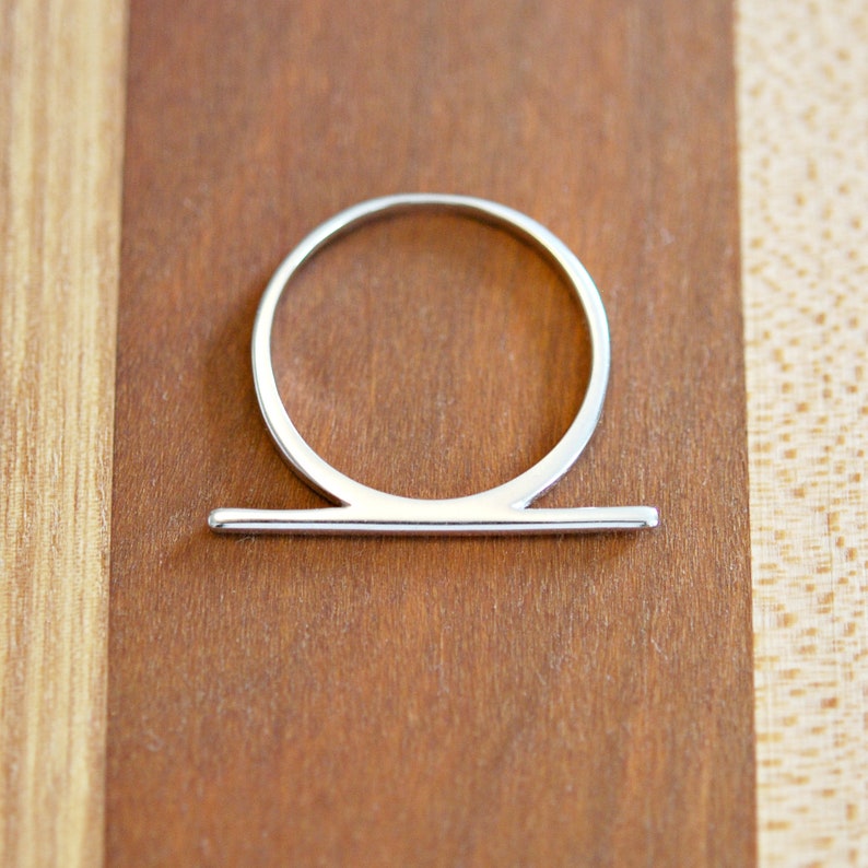 Peut inclure: Une bague en argent avec une bande fine et une barre horizontale en haut.