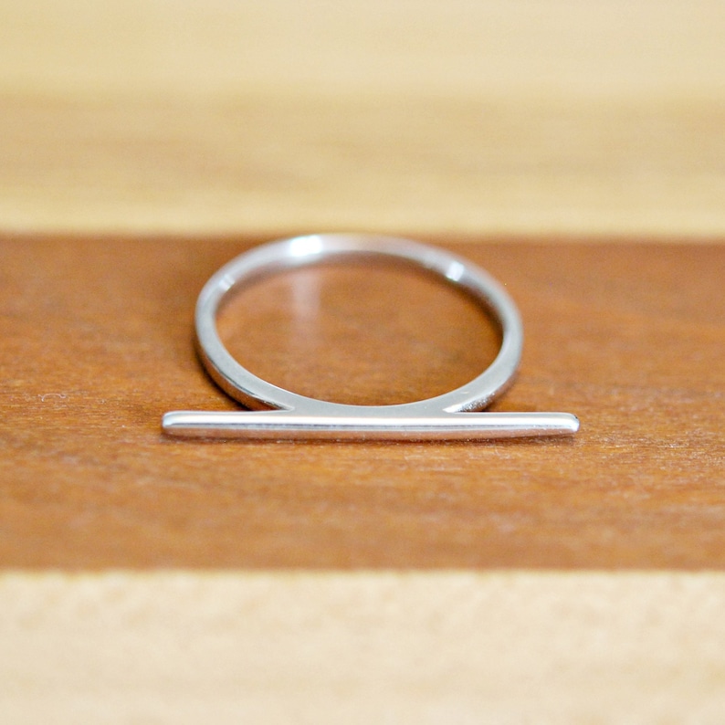 Peut inclure: Une bague en argent avec une fine barre horizontale en haut.