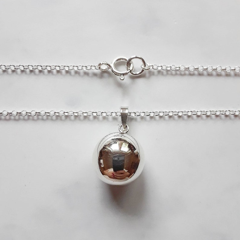 May include: A silver chain necklace with a round, silver pendant. The pendant is smooth and shiny.