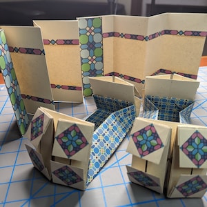 May include: A set of origami boxes with a geometric pattern in shades of blue, green, and pink. The boxes are folded from paper and have a unique design.