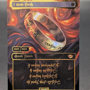 Peut inclure: Une carte à collectionner représentant un anneau doré avec une inscription gravée sur un fond de flammes orange et noires tourbillonnantes. La carte affiche le texte 001/001, divers symboles et des lignes d'écriture dorée dans un encadré sombre.