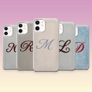 Puede incluir: Cinco fundas para smartphone con un acabado de tela texturizada, cada una con una letra bordada en cursiva. Las fundas muestran las letras N, R, M, L y D en varios colores de hilo, incluyendo bordados en rojo oscuro, azul claro y granate.