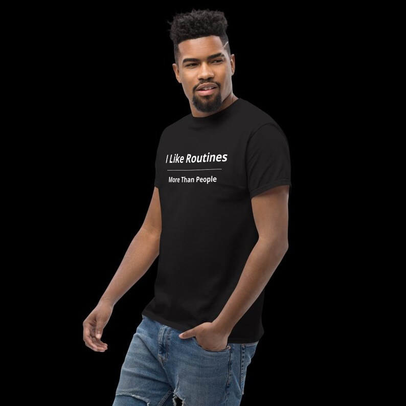 K&ouml;nnte beinhalten: Ein schwarzes kurz&auml;rmeliges T-Shirt mit dem wei&szlig;en Text "I Like Routines" &uuml;ber einer horizontalen Linie und dem Text "More Than People" direkt darunter. Das T-Shirt wird mit einer blauen Jeans aus Denim kombiniert.