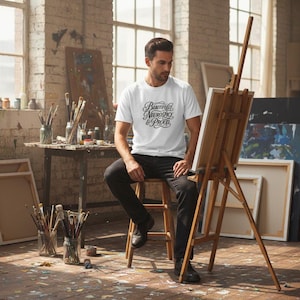 K&ouml;nnte beinhalten: Ein wei&szlig;es Kurzarm-T-Shirt mit dem schwarzen Schriftzug "Beautifully Neurospicy & Proud" in einer dekorativen Schreibschrift. Das Shirt wird mit einer schwarzen Hose kombiniert und sorgt f&uuml;r einen schlichten Look im Alltag.