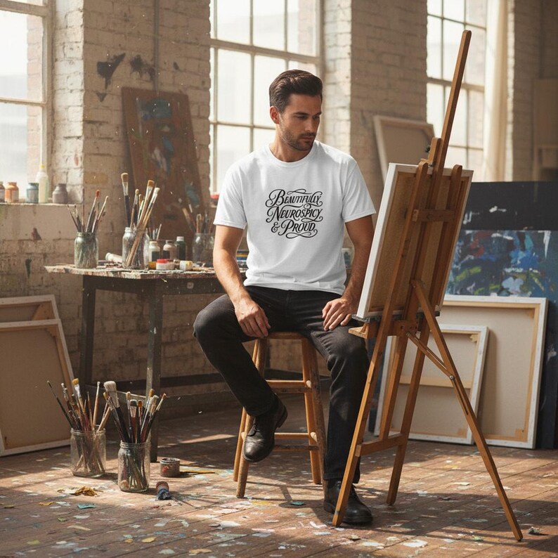K&ouml;nnte beinhalten: Ein wei&szlig;es Kurzarm-T-Shirt mit dem schwarzen Schriftzug "Beautifully Neurospicy & Proud" in einer dekorativen Schreibschrift. Das Shirt wird mit einer schwarzen Hose kombiniert und sorgt f&uuml;r einen schlichten Look im Alltag.