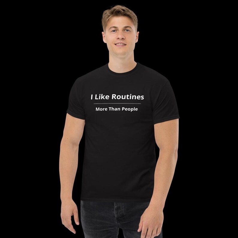 K&ouml;nnte beinhalten: Ein schwarzes Kurzarm-T-Shirt mit dem wei&szlig;en Text "I Like Routines" &uuml;ber einer horizontalen Linie, wobei der Text "More Than People" direkt unter der Linie in einer klaren, serifenlosen Schrift mittig auf der Brust gedruckt ist.