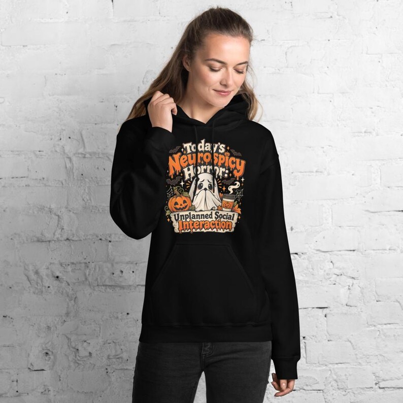 K&ouml;nnte beinhalten: Ein schwarzer Kapuzenpullover mit einem Grafikdruck und dem Text Today's Neurospicy Horror: Unplanned Social Interaction. Das Design zeigt ein wei&szlig;es Gespenst, einen orangefarbenen K&uuml;rbis und einen Kaffeebecher, umgeben von Flederm&auml;usen.