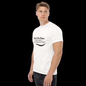 Puede incluir: Una camiseta blanca de manga corta con texto negro en la parte delantera que dice I Don't Do Chaos I Just Clean Up Yours, acompa&ntilde;ado de adornos decorativos y una l&iacute;nea gr&aacute;fica curva debajo del texto, sobre un fondo liso.