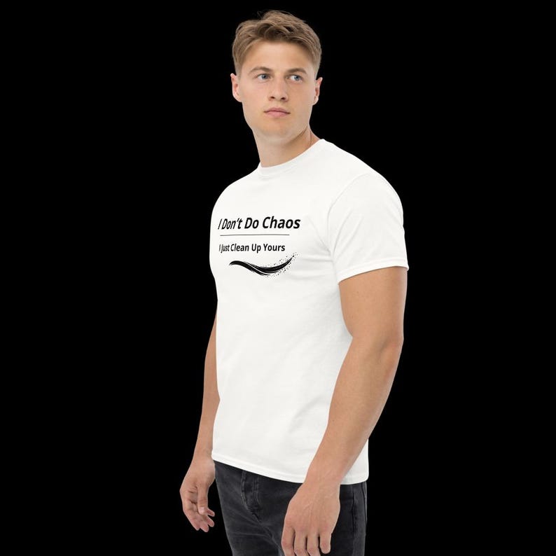 Op de afbeelding: Een wit T-shirt met korte mouwen voorzien van de zwarte tekst "I Don't Do Chaos" boven de tekst "I Just Clean Up Yours" met een zwart grafisch swoosh-ontwerp onder de letters, gedragen met een donkergrijze spijkerbroek.