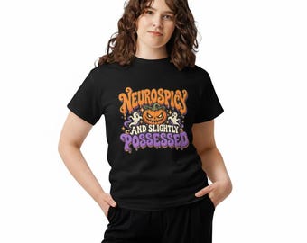 May include: A black short-sleeved t-shirt featuring a graphic print with the text "Neurospicy and slightly possessed" in orange and purple. The design includes a central jack-o'-lantern pumpkin and two small white ghosts.
