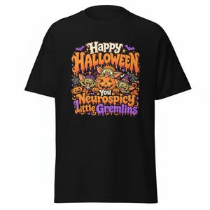 May include: A black t-shirt featuring a colorful graphic with three cartoon gremlins and pumpkins. The text reads Happy Halloween You Neurospicy Little Gremlins in orange and purple lettering, surrounded by spiderwebs, bats, and autumn leaves.