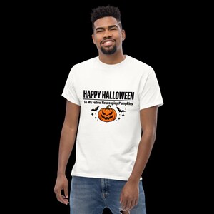 K&ouml;nnte beinhalten: Ein wei&szlig;es kurz&auml;rmeliges T-Shirt mit dem schwarzen Text HAPPY HALLOWEEN To My Fellow Neurospicy Pumpkins, zentriert &uuml;ber einer Grafik eines orangefarbenen K&uuml;rbisses mit gezacktem Grinsen, flankiert von zwei kleinen schwarzen Flederm&auml;usen und Sternen.