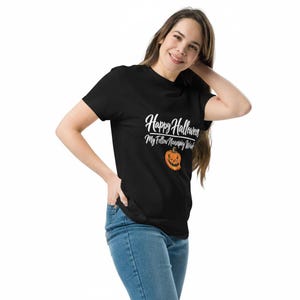 May include: A black short-sleeved t-shirt featuring white text that reads Happy Halloween My Fellow Neurospicy Witches above an orange jack-o'-lantern graphic with a jagged, toothy grin and blue denim jeans.