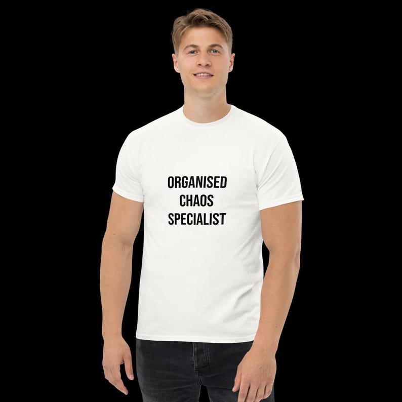 May include: A white short-sleeved t-shirt featuring the black text "ORGANISED CHAOS SPECIALIST" printed in a bold, sans-serif font across the centre of the chest. The garment has a classic crew neckline and a standard fit, made of plain fabric.
