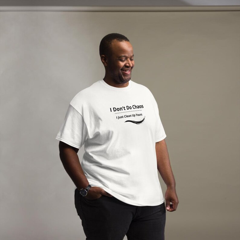 Op de afbeelding: Een wit T-shirt met korte mouwen en de zwarte tekst I Don't Do Chaos I Just Clean Up Yours met een decoratieve zwarte swoosh-afbeelding onder de tekst, gedragen met een zwarte broek en een zwart horloge om de linkerpols.