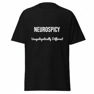 Könnte beinhalten: Ein schwarzes Kurzarm-T-Shirt mit dem Wort NEUROSPICY in fetten weißen Großbuchstaben auf der Brust und dem darunter in weißer Schreibschrift gedruckten Satz Unapologetically Different. Das Kleidungsstück hat einen Rundhalsausschnitt.