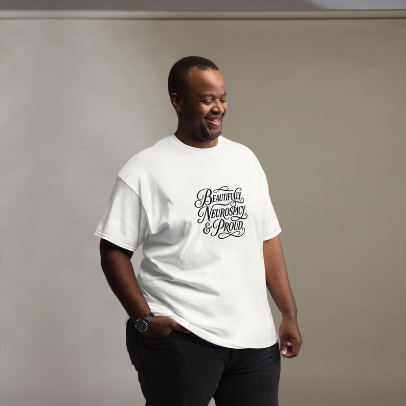 K&ouml;nnte beinhalten: Ein wei&szlig;es kurz&auml;rmeliges T-Shirt mit schwarzem Schreibschrift-Text auf der Brust, der "Beautifully Neurospicy & Proud" lautet. Das Shirt hat einen Rundhalsausschnitt und eine Standardpassform, kombiniert mit einer schwarzen Hose und einer Armbanduhr.