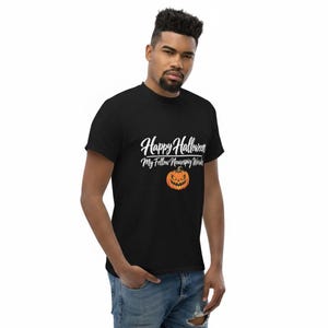 May include: A black short-sleeved t-shirt featuring the white text "Happy Halloween My Fellow Neurospicy Weirdos" printed above a graphic of an orange jack-o'-lantern pumpkin with a jagged, menacing facial expression and a dark green stem.