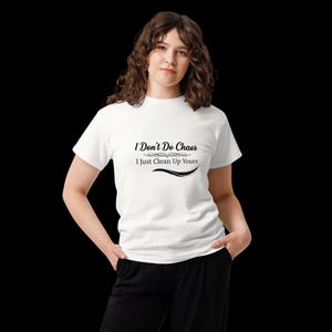 Puede incluir: Una camiseta blanca de manga corta con el texto impreso en negro I Don't Do Chaos I Just Clean Up Yours con adornos decorativos encima y debajo de la segunda l&iacute;nea de texto, combinada con pantalones negros sobre un fondo negro.