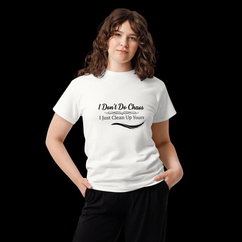 Puede incluir: Una camiseta blanca de manga corta con el texto impreso en negro I Don't Do Chaos I Just Clean Up Yours con adornos decorativos encima y debajo de la segunda l&iacute;nea de texto, combinada con pantalones negros sobre un fondo negro.