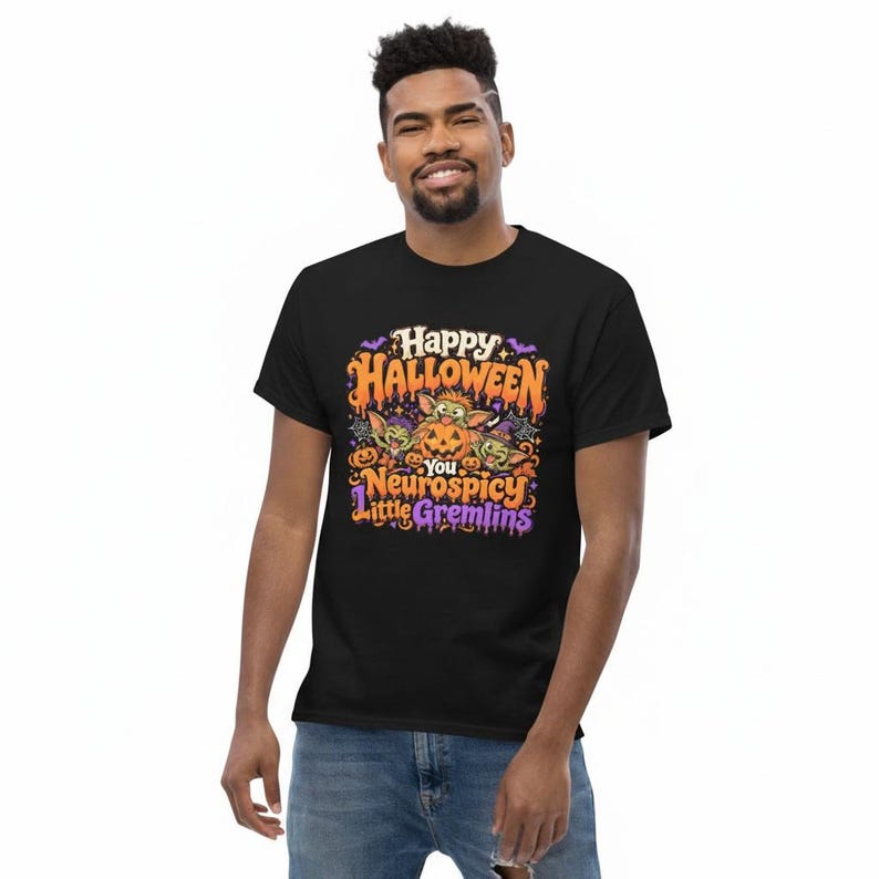 May include: A black short-sleeve t-shirt featuring a colorful graphic print with orange, purple, and green accents. The text reads Happy Halloween You Neurospicy Little Gremlins, accompanied by illustrations of small green creatures and pumpkins.