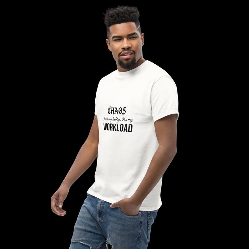 May include: A white short-sleeved t-shirt featuring black text on the chest that reads "CHAOS isn't my hobby, it's my WORKLOAD" in a mix of gothic and bold sans-serif fonts. The shirt is paired with blue denim jeans.