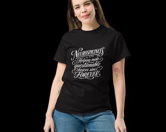 May include: A black short-sleeved t-shirt featuring white cursive text that reads: Neurospiciness Helping make questionable choices since FOREVER. The shirt is paired with blue denim jeans, creating a casual look with a bold graphic design.