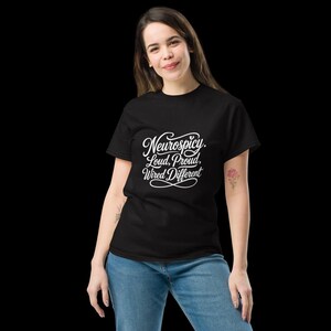 K&ouml;nnte beinhalten: Ein schwarzes kurz&auml;rmeliges T-Shirt mit wei&szlig;em Schreibschrift-Text auf der Brust, der lautet: Neurospicy. Loud, Proud, Wired Different. Das T-Shirt hat einen Rundhalsausschnitt und wird mit einer blauen Jeans kombiniert, was einen l&auml;ssigen Look ergibt.