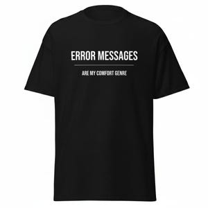 Peut inclure: Un t-shirt noir à manches courtes avec du texte blanc imprimé sur la poitrine. Le texte indique ERROR MESSAGES dans une grande police, suivi d'une ligne horizontale et de la phrase ARE MY COMFORT GENRE dans une police plus petite.